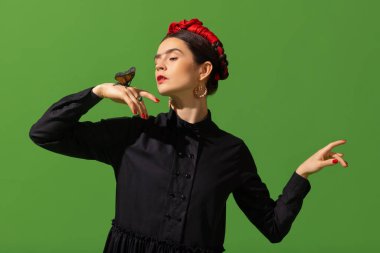 Close-up young beautiful woman in image of famous painter, artist Frida Kahlo on green background. Retro style, comparison of eras concept.