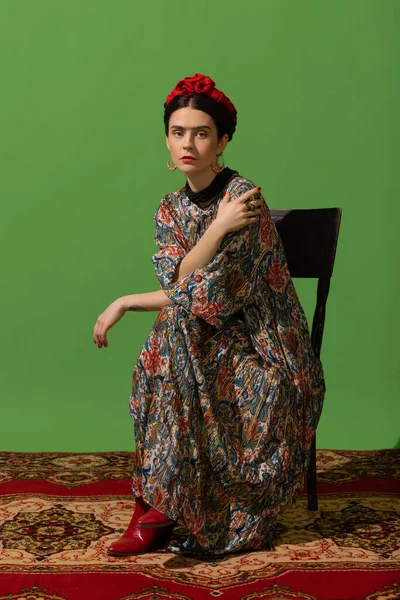 Portrait of young woman in image of famous painter, artist Frida Kahlo on green background. Comparison of eras — Zdjęcie stockowe