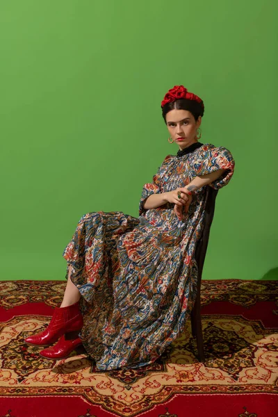 Portrait of young woman in image of famous painter, artist Frida Kahlo on green background. Comparison of eras — Stock Photo, Image