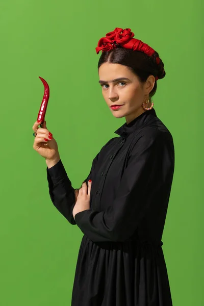 Young beautiful woman in image of famous painter, artist Frida Kahlo on green background. Retro style, comparison of eras concept. — Fotografia de Stock