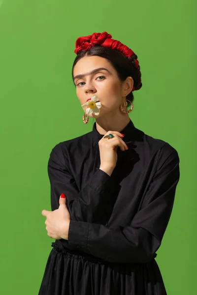 Close-up young beautiful woman in image of famous painter, artist Frida Kahlo on green background. Retro style, comparison of eras concept. — Stok fotoğraf