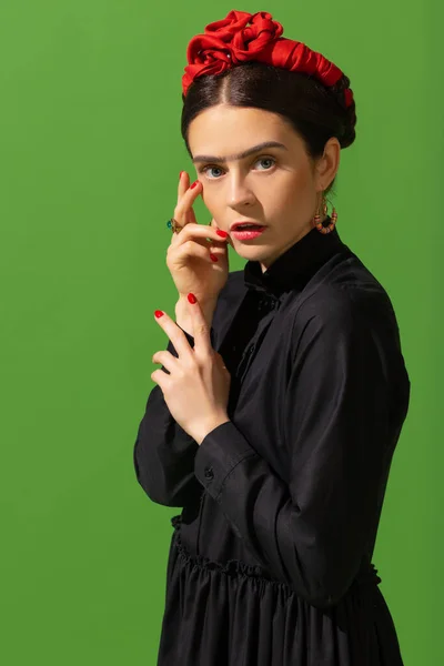 Close-up young beautiful woman in image of famous painter, artist Frida Kahlo on green background. Retro style, comparison of eras concept. — Fotografia de Stock