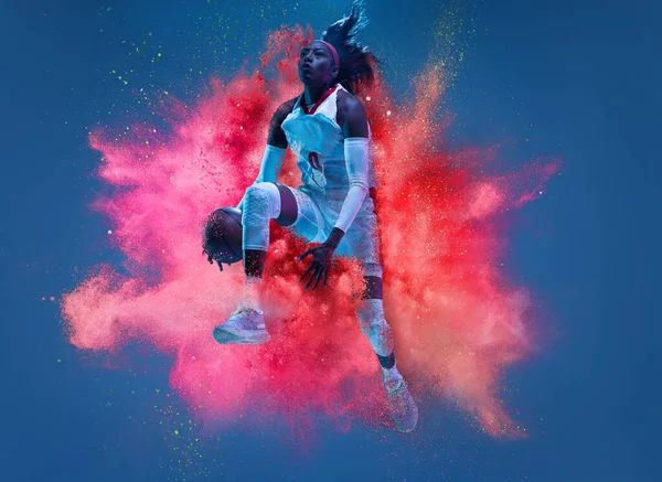 One young woman sportsman basketball player in explosion of colored neon powder isolated on dark blue background — Stockfoto