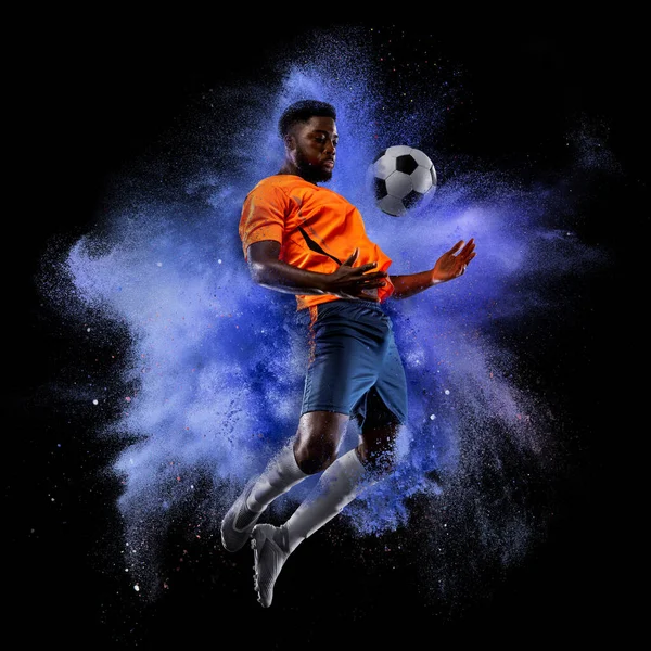 One young sportsman soccer football player in explosion of colored neon powder isolated on dark background — Zdjęcie stockowe