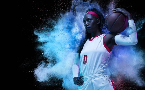 One young woman sportsman basketball player in explosion of colored neon powder isolated on dark background —  Fotos de Stock