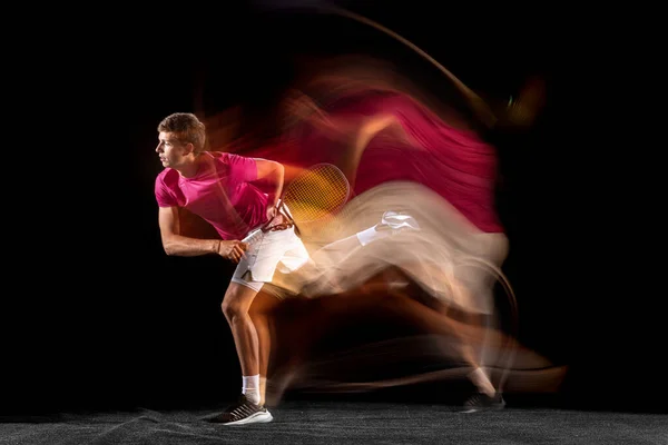Young caucasian male tennis player playing tennis in mixed light on dark background. Concept of healthy lifestyle, professional sport, hobby. — Stock fotografie