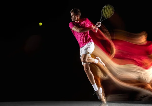 Young caucasian male tennis player playing tennis in mixed light on dark background. — Photo
