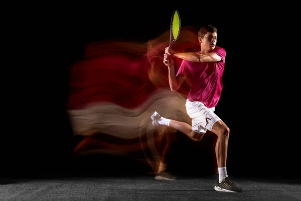 Young caucasian male tennis player playing tennis in mixed light on dark background. — Stock Fotó