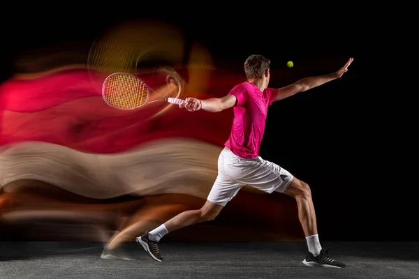 Young caucasian male tennis player playing tennis in mixed light on dark background. Back view — Fotografia de Stock