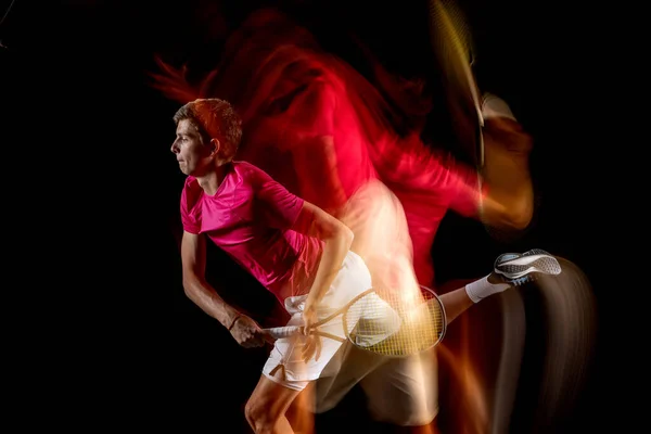 Young caucasian male tennis player playing tennis in mixed light on dark background. — ストック写真