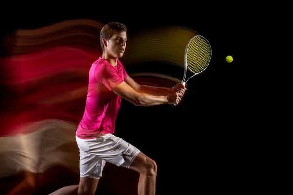 Young caucasian male tennis player playing tennis in mixed light on dark background. Concept of healthy lifestyle, professional sport, hobby. — Stock Fotó