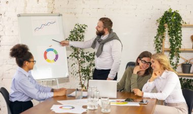 Genç erkek ve kadınlar, modern ofiste birlikte çalışan meslektaşlar görüşmeler sırasında cihazlar ve aletler kullanıyorlar.