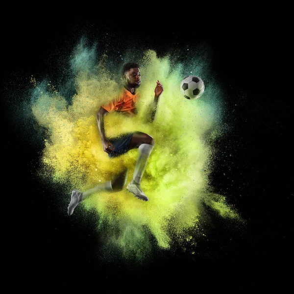 Junge afrikanische Sportler Fußballspieler in Explosion von gelbem Neonpulver isoliert auf dunklem Hintergrund — Stockfoto