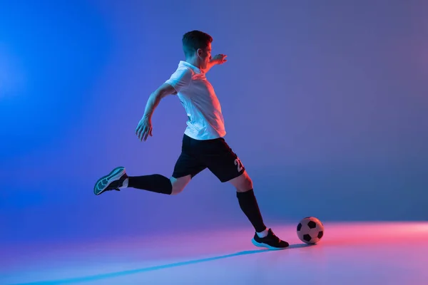 Een mannelijke voetballer in actie en beweging geïsoleerd op gradiënt blauw roze achtergrond in neon licht — Stockfoto