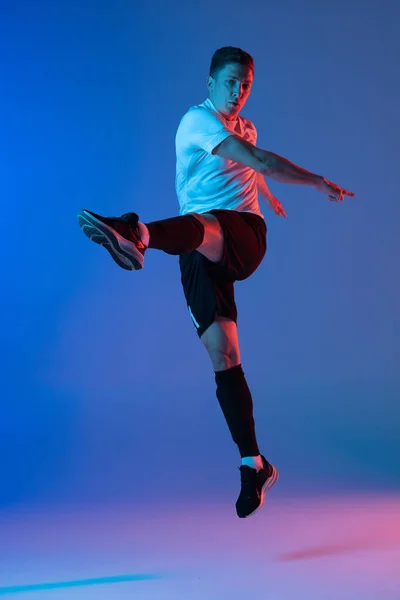 Jonge blanke man, mannelijke voetballer oefenen geïsoleerd op verloop blauw roze achtergrond in neon licht — Stockfoto