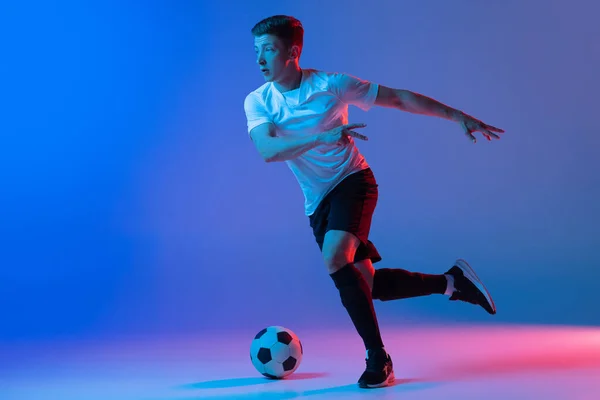 Hombre joven caucásico, entrenamiento de jugador de fútbol masculino aislado sobre fondo rosa azul degradado en luz de neón —  Fotos de Stock