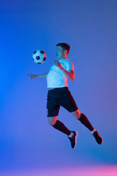 Bir erkek futbol oyuncusu hareket halinde ve hareket halinde. Neon ışıklarıyla izole edilmiş mavi bir arka planda. — Stok fotoğraf