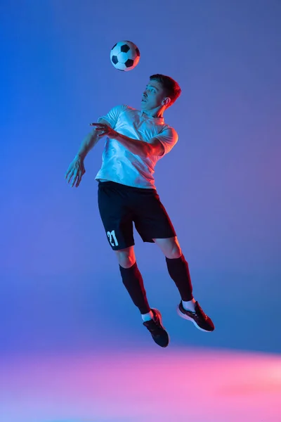 Jonge blanke man, mannelijke voetbalspeler springen geïsoleerd op gradiënt blauw roze achtergrond in neon licht. Achteraanzicht — Stockfoto