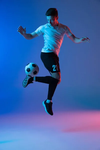 Um jogador de futebol masculino em ação e movimento isolado no gradiente azul rosa fundo em luz de néon — Fotografia de Stock