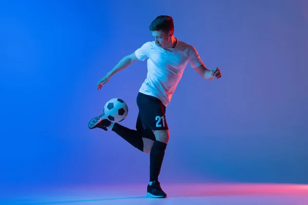 Een mannelijke voetballer in actie en beweging geïsoleerd op gradiënt blauw roze achtergrond in neon licht — Stockfoto