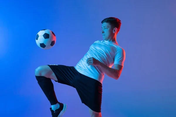 Jonge blanke man, mannelijke voetbal speler training geïsoleerd op gradiënt blauw roze achtergrond in neon licht — Stockfoto