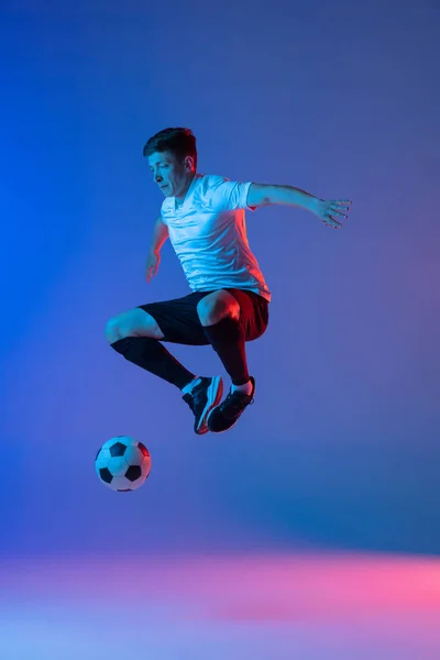 Jovem caucasiano homem, futebol masculino jogador de treinamento isolado no gradiente azul rosa fundo em luz de néon — Fotografia de Stock