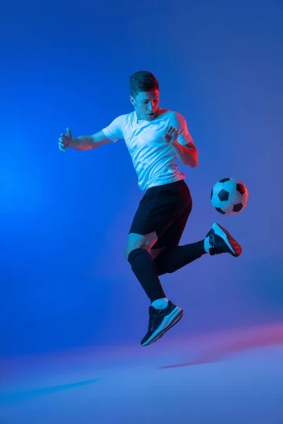 Jovem homem caucasiano, jogador de futebol masculino saltando isolado no gradiente azul rosa fundo em luz de néon — Fotografia de Stock