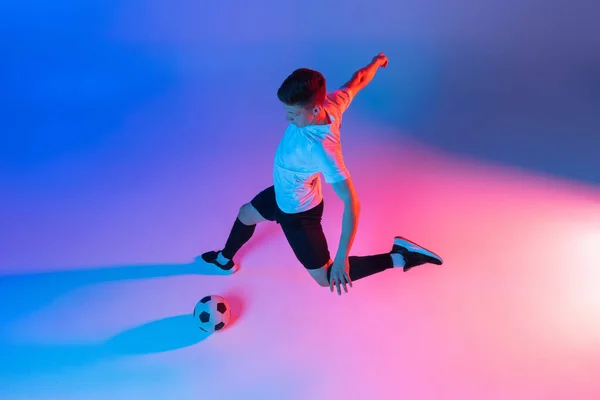 Magas látószögű kilátás fiatal férfi, férfi focista képzés elszigetelt gradiens kék rózsaszín háttér neon fény. — Stock Fotó