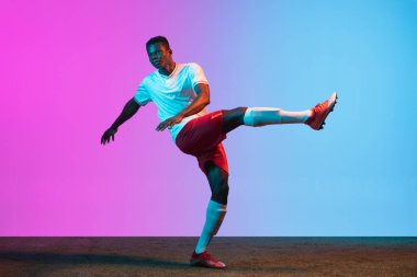 Bir Afrikalı, profesyonel futbolcu eğitimi neon ışıklarıyla izole edilmiş mavi bir arka planda..