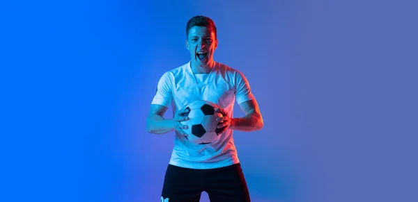 Retrato de meia-distância de jogador de futebol profissional de pé isolado em gradiente azul fundo rosa em luz de néon. Conceito de esporte, beleza. — Fotografia de Stock
