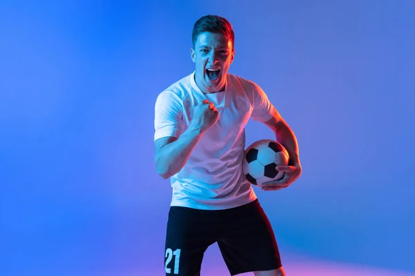 Retrato de meia-distância de jogador de futebol profissional de pé isolado em gradiente azul fundo rosa em luz de néon. Conceito de esporte, beleza. — Fotografia de Stock