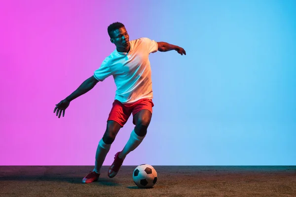 Bir Afrikalı, profesyonel futbolcu eğitimi neon ışıklarıyla izole edilmiş mavi bir arka planda.. — Stok fotoğraf