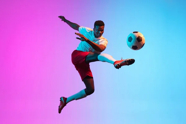 Um homem africano, treinamento de jogador de futebol profissional isolado em gradiente azul rosa fundo em luz de néon. — Fotografia de Stock