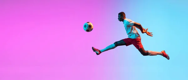 O Flyer. Um homem africano, treinamento de jogador de futebol profissional isolado em gradiente azul rosa fundo em luz de néon. — Fotografia de Stock