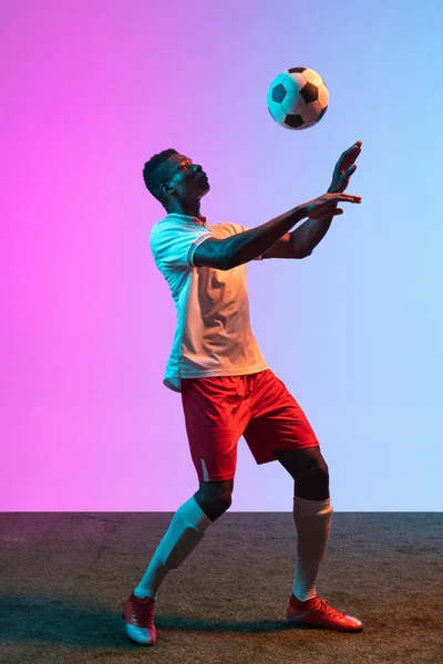 Portrait d'un footballeur professionnel africain isolé sur fond rose bleu dégradé au néon. — Photo