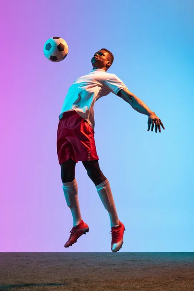 霓虹灯下，非洲职业足球运动员在渐变蓝色粉红背景下独立站立的肖像. — 图库照片