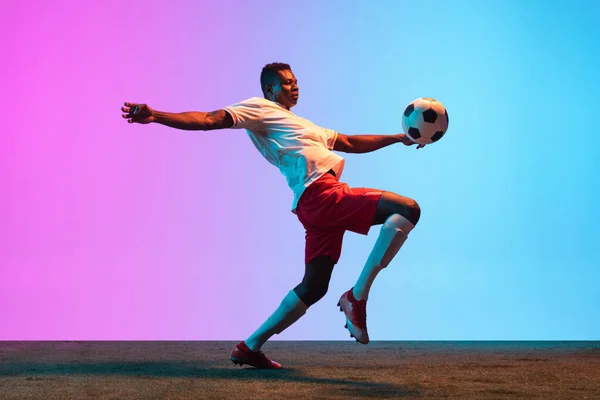 Afrikalı profesyonel futbolcunun portresi neon ışıklarıyla izole edilmiş mavi bir arkaplanda duruyor.. — Stok fotoğraf