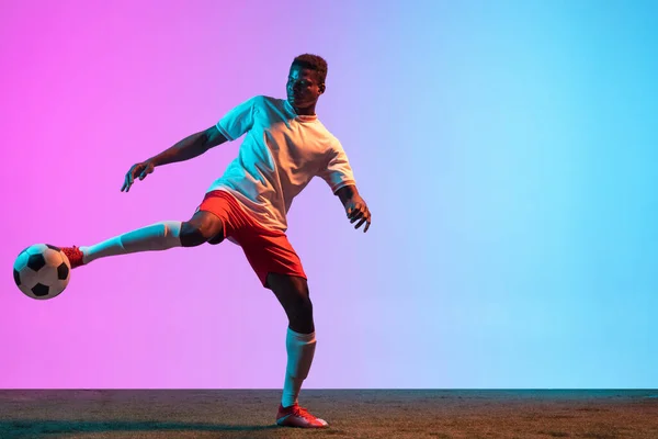Afrikalı profesyonel futbolcunun portresi neon ışıklarıyla izole edilmiş mavi bir arkaplanda duruyor.. — Stok fotoğraf