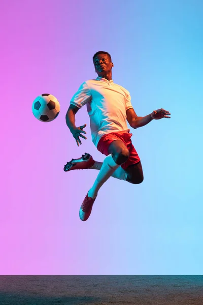 Portrait of African professional football player standing isolated on gradient blue pink background in neon light. Back view — Stock Photo, Image
