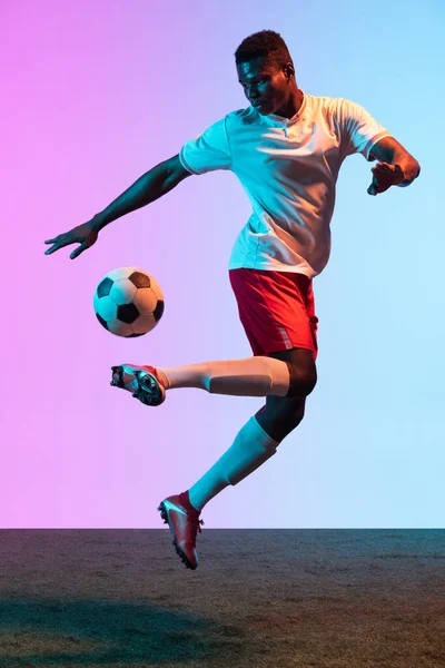 Portrait d'un footballeur professionnel africain isolé sur fond rose bleu dégradé au néon. Vue arrière — Photo