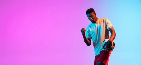 Africano homem, jogador de futebol profissional de pé isolado no gradiente azul rosa fundo em luz de néon. — Fotografia de Stock