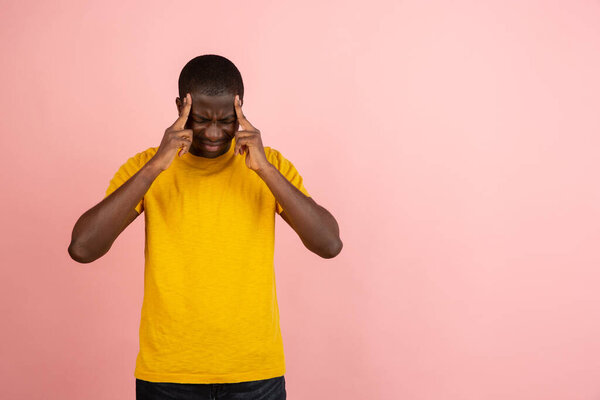 Stressed young african american man feel pain and having terrible strong headache concept. Tired upset black guy massaging temples and suffering from migraine isolated on pink studio blank background