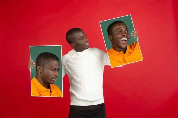 Jovem homem africano segurando seus retratos isolados sobre fundo estúdio vermelho com copyspace para anúncio. — Fotografia de Stock