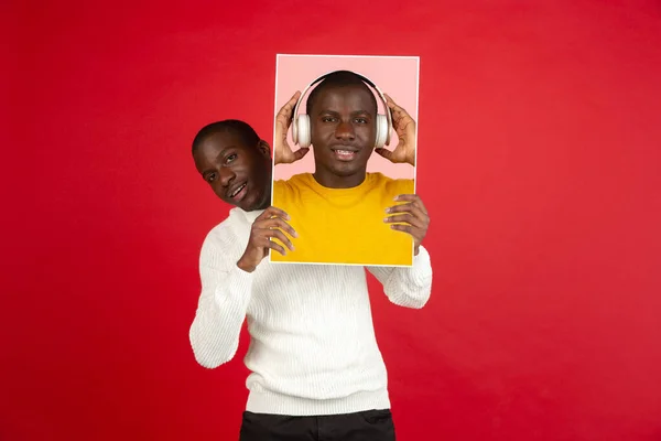 Jovem homem africano segurando seu retrato isolado sobre fundo estúdio vermelho com copyspace para anúncio. — Fotografia de Stock