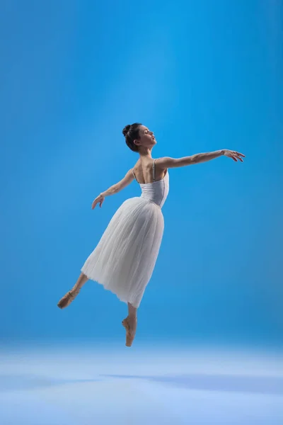 Joven y elegante bailarina de ballet aislada sobre fondo de estudio azul. Arte, movimiento, acción, flexibilidad, concepto de inspiración. — Foto de Stock