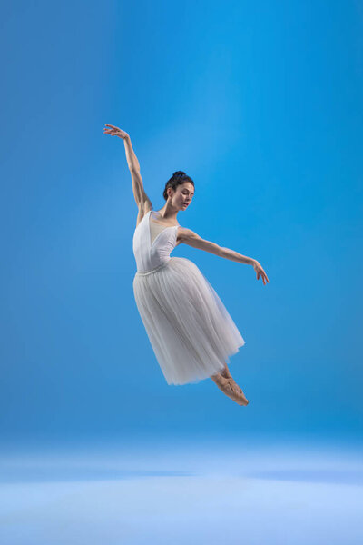 Young and graceful ballet dancer isolated on blue studio background. Art, motion, action, flexibility, inspiration concept.