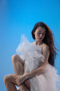 Mavi stüdyo arka planında oturan yorgun balerin.