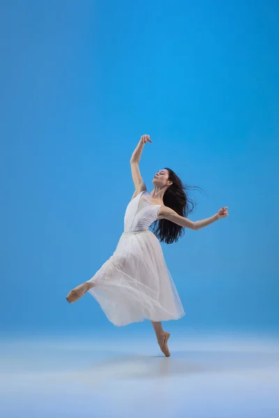 Молодая и невероятно красивая балерина позирует и танцует в синей студии, полной света. — стоковое фото