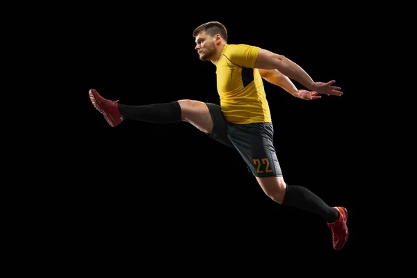 Poderoso, volando sobre el campo. Fútbol joven, jugador de fútbol en acción, movimiento aislado sobre fondo negro . — Foto de Stock
