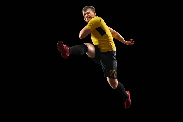 Poderoso, volando sobre el campo. Fútbol joven, jugador de fútbol en acción, movimiento aislado sobre fondo negro . — Foto de Stock